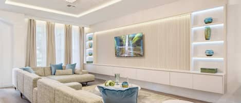 A modern living room with a sectional sofa, a round coffee table, and a flat-screen TV mounted on a wall with built-in shelving.