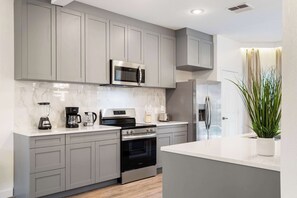 A modern kitchen with grey cabinets, a stainless steel oven, a microwave, and a refrigerator. - Mario, Mickey & Jedi Arcade Villa w/ Themed Rooms (Kissimmee)