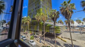 A modern building with a curved glass facade, surrounded by palm trees and a clear blue sky. - Apartment Las Canteras Beachfront Views (Las Palmas de Gran Canaria)