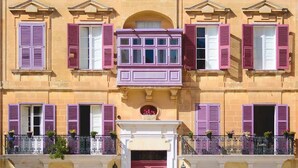 Ein Gebäude mit mehreren Fenstern, einige mit Rollläden, und einem Balkon mit schmiedeeisernen Geländern.