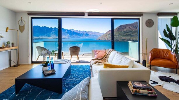 Un salón moderno con un gran ventanal corredera que da a un balcón con vistas a la montaña.