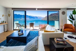 Un salón moderno con un gran ventanal corredera que da a un balcón con vistas a la montaña.