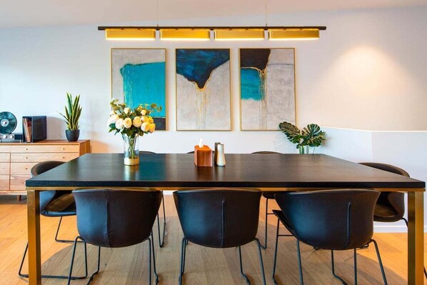 Un comedor moderno con una mesa larga, sillas negras y tres cuadros abstractos en la pared.