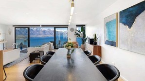 Un comedor moderno con una larga mesa, sillas negras y vistas a montañas y una masa de agua a través de amplios ventanales.