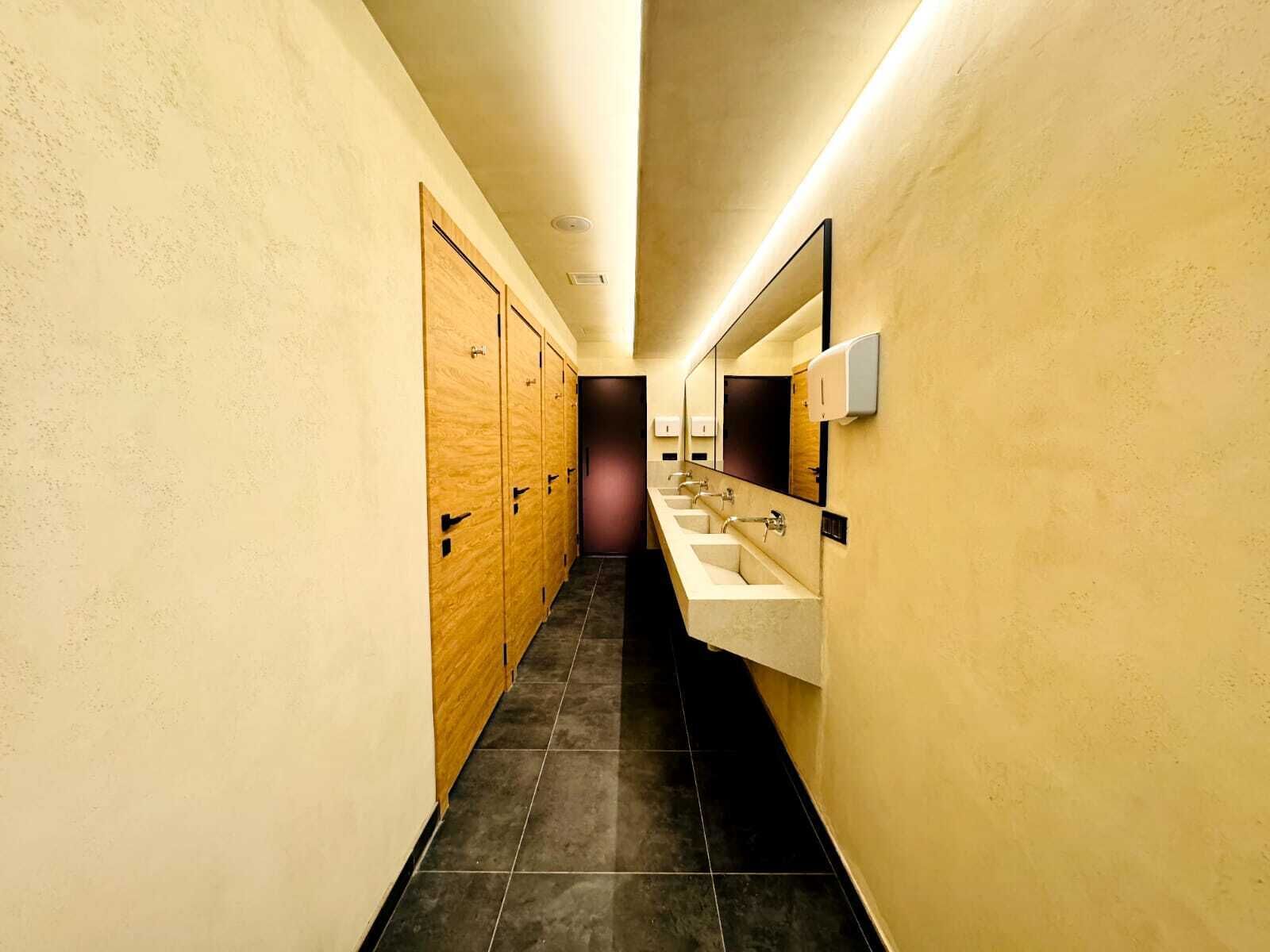 A narrow hallway with wooden lockers on one side and a row of sinks with mirrors on the other.