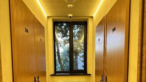 Un pasillo estrecho con taquillas de madera, alfombra estampada, una ventana con vistas a árboles y un radiador.
