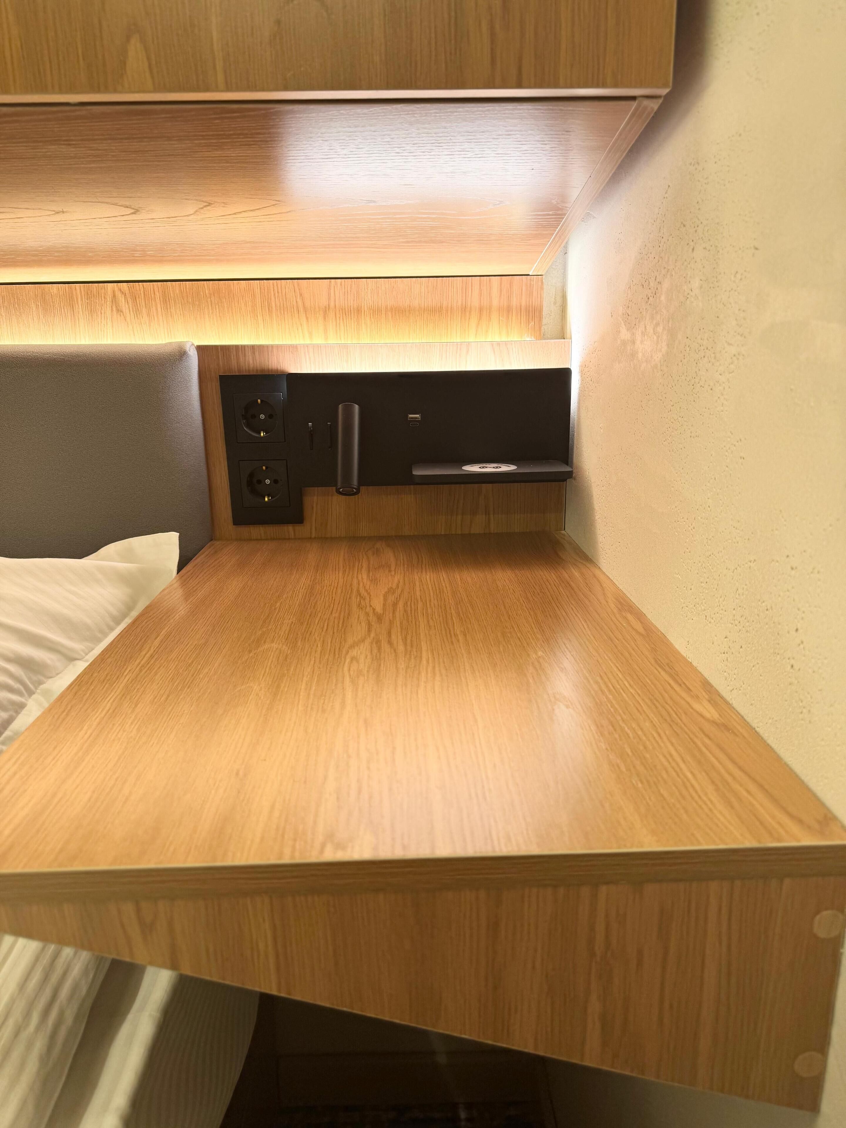 A compact kitchenette with a wooden countertop, two electrical outlets, a USB port, and a small shelf.