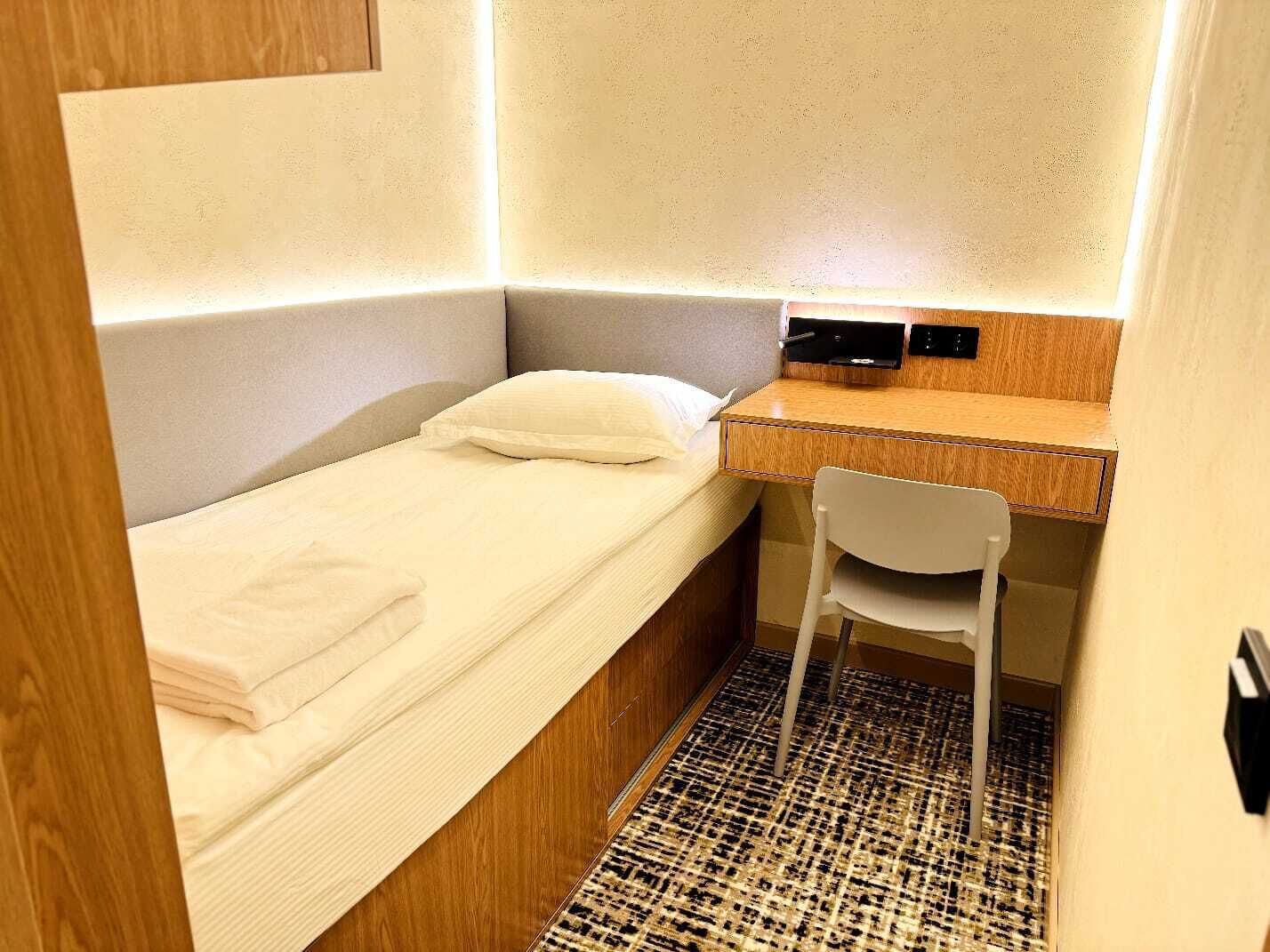 A small, compact bedroom with a single bed, a desk, and a chair.