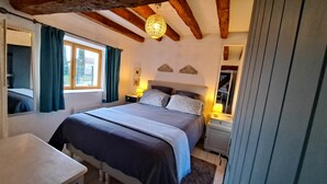 Een slaapkamer met een groot bed, een nachtkastje, een lamp, een spiegel en een raam met gordijnen.