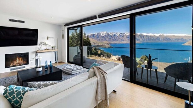 A modern living room with a fireplace, a sofa, and a large sliding glass door leading to a balcony with a mountain view.