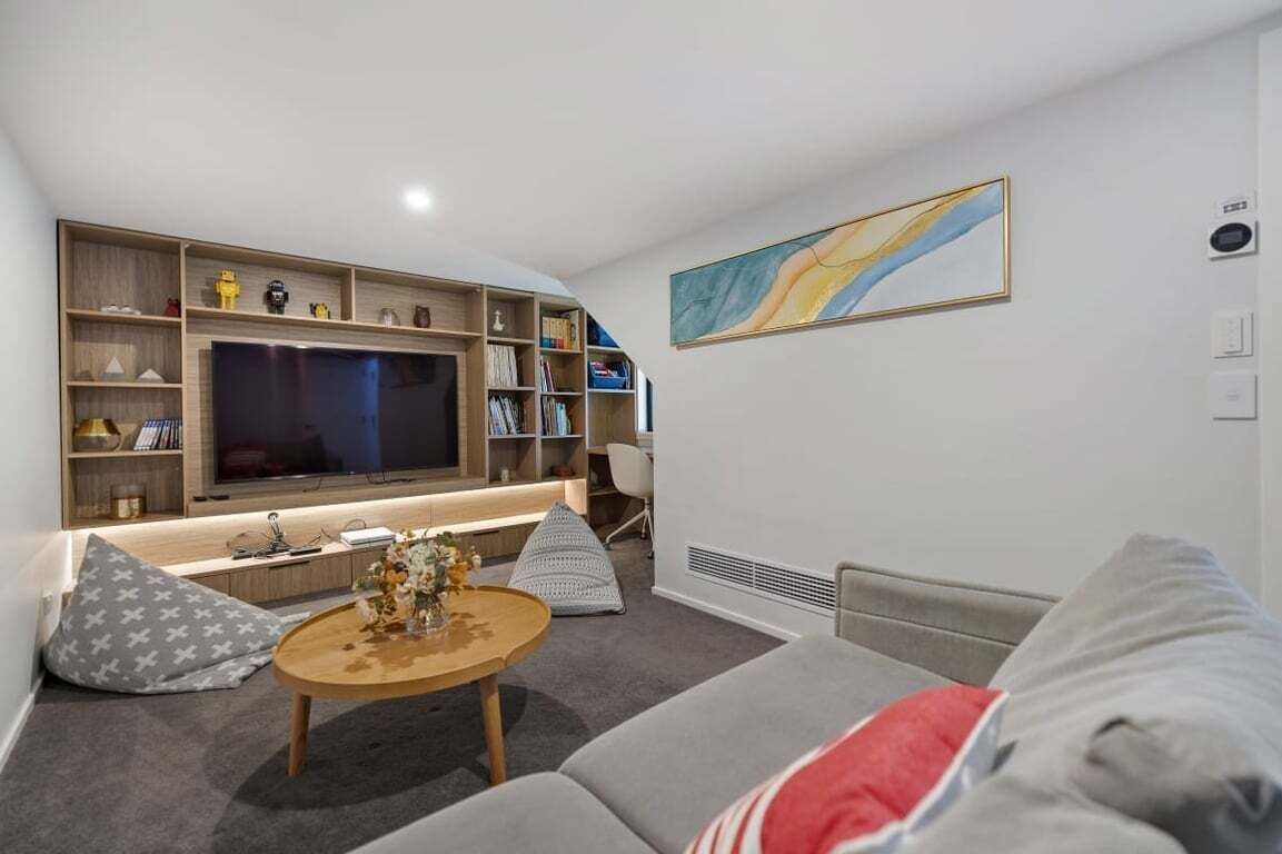 A modern living room with a large flat-screen TV, built-in shelves, a comfortable sofa, and a coffee table.