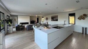 A modern kitchen with a large island, a dining area with a sofa and chairs, and a living room with a fireplace. - Modern villa, fast WiFi, A/C, pool in private backyard, ideal for fun and work (Vallauris)