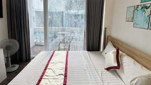 A hotel room with a large bed, a standing fan, a balcony with curtains, and a view of the cityscape. - B Homeaway Bui Vien (Ho Chi Minh City)