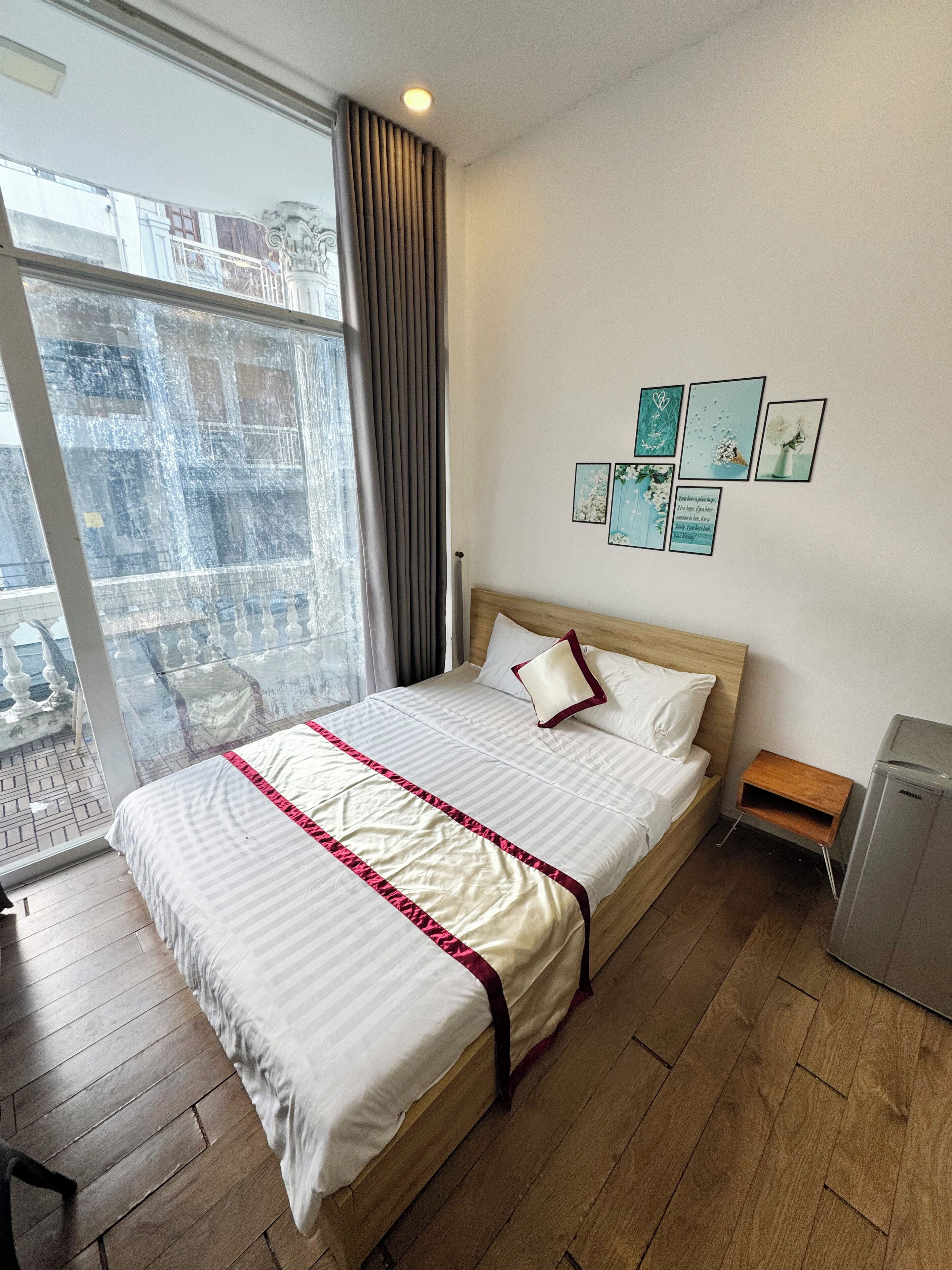 Une chambre d’hôtel avec un grand lit, un plancher en bois, une petite table de chevet, un climatiseur fixé au mur et un balcon avec vue sur la ville.