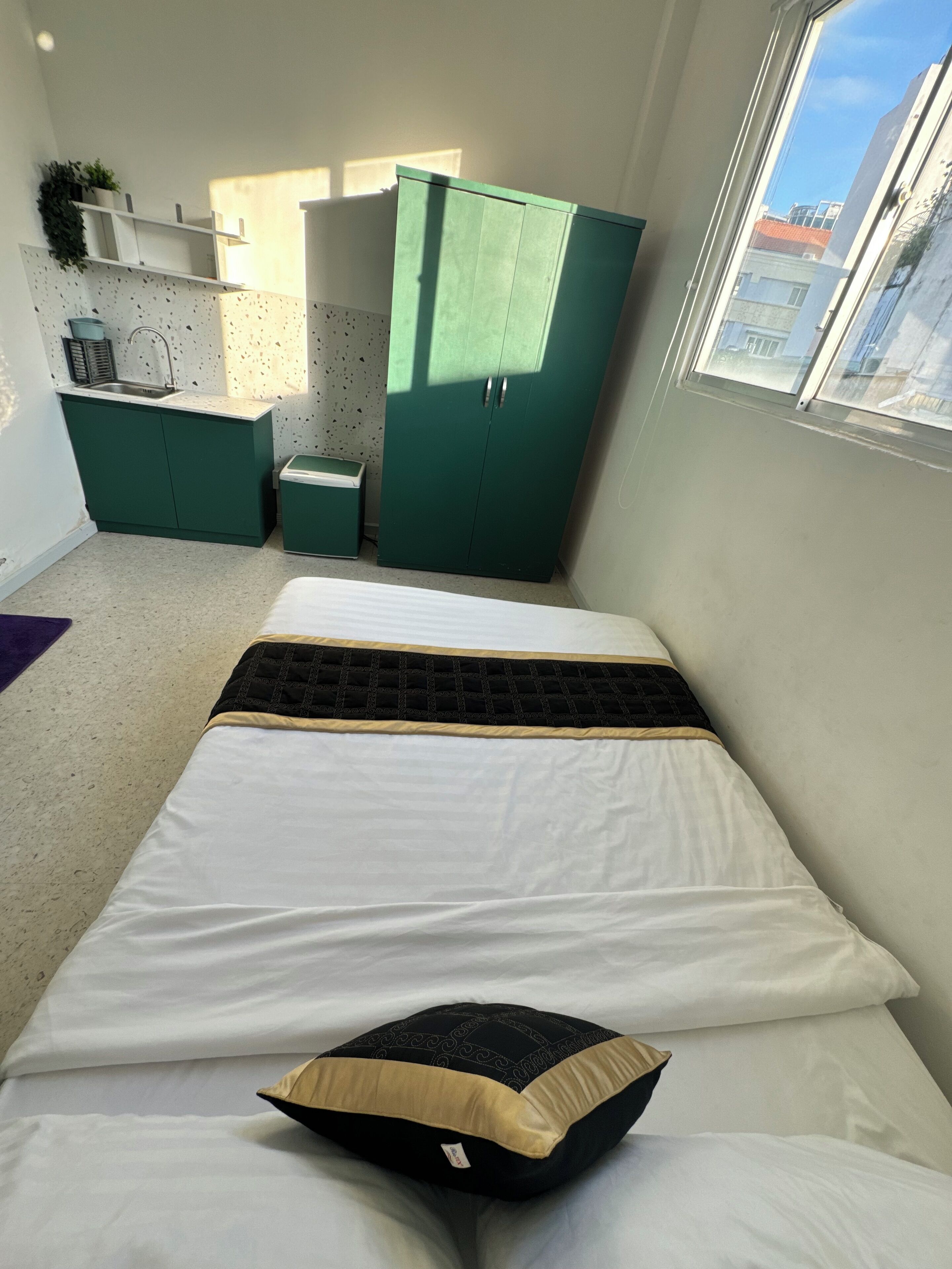 Una habitación pequeña con cama, kitchenette y ventana.
