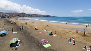 Une plage où l’on peut voir des gens bronzer et se baigner, des parasols et un ciel dégagé.