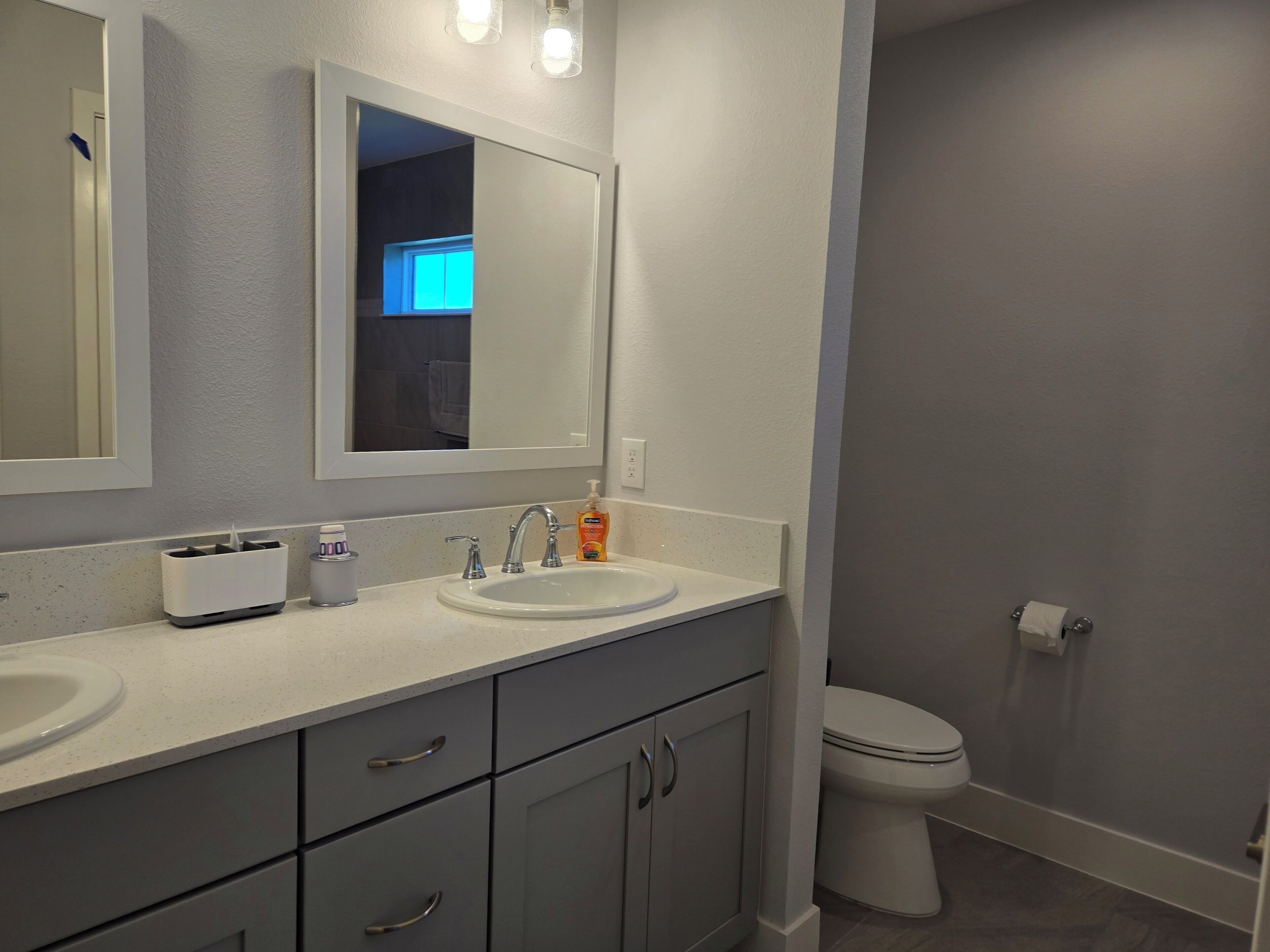 A modern bathroom with two sinks, a mirror, and a toilet.