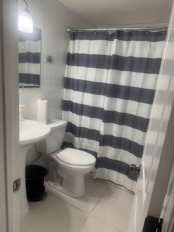 A bathroom with a white toilet, a sink, and a striped shower curtain. - La sama Wynwood (Miami)