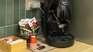 A kitchen with a coffee machine, a basket of coffee pods, a box of coffee cups, and a wooden counter. - B&B MARGIÒ  (Fiumicino)
