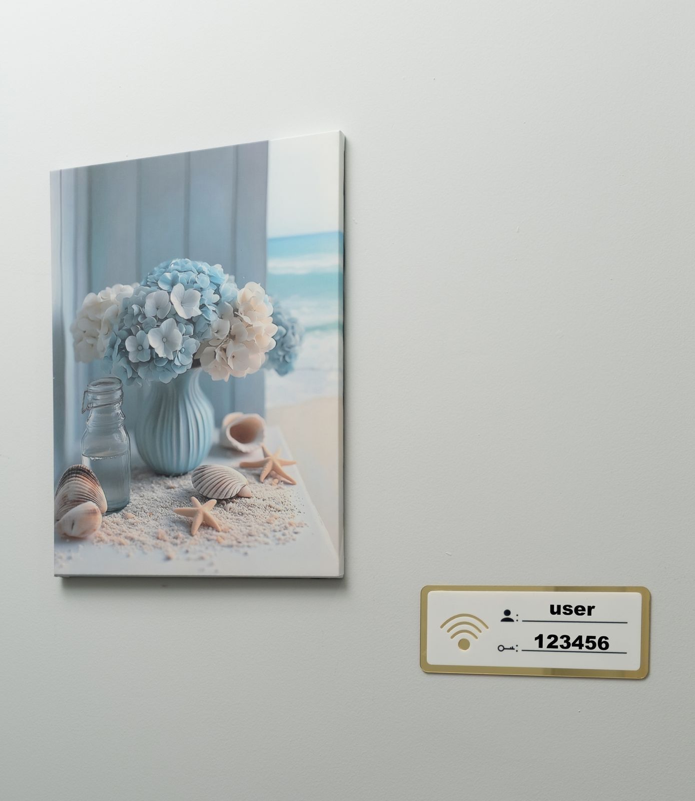 A framed artwork of a seaside scene with flowers, shells, and starfish on a table.