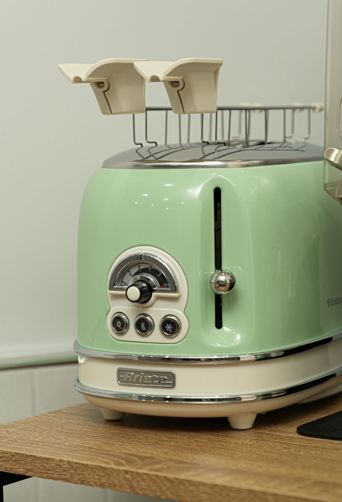A vintage green and white toaster with a dial and buttons on the front, placed on a wooden surface.