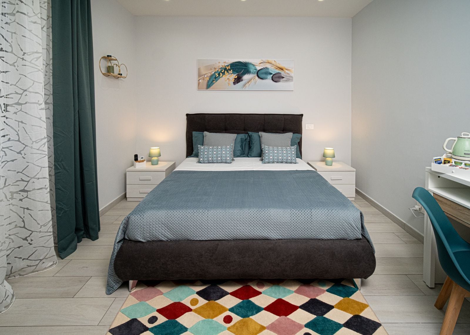 A bedroom with a bed, nightstands, a desk, and a colorful rug.