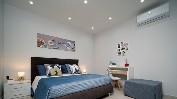 A modern bedroom with a bed, bedside tables, a desk, and an air conditioning unit. - B&B MARGIÒ  (Fiumicino)