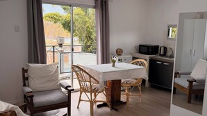 A room with a dining table, chairs, a kitchen area, and a view through a window. - Monoambiente El Arrayán (Echeverry)