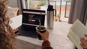 Una persona usando una computadora portátil en una mesa con vistas a edificios y un balcón.