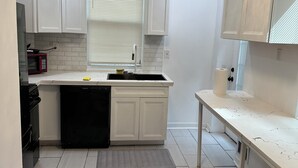 A modern kitchen with white cabinets, a black dishwasher, and a white countertop. - Charming 4-bedroom house with WiFi and AC in Pittsburgh (Pittsburgh)