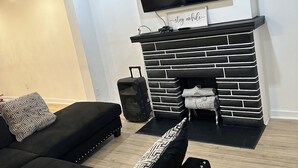 A modern living room with a black and white fireplace, a flat-screen TV mounted above it, and two black sofas with patterned cushions. - Charming 4-bedroom house with WiFi and AC in Pittsburgh (Pittsburgh)