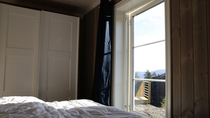 Een slaapkamer met een bed, een witte kledingkast en een glazen schuifdeur die uitkomt op een buitenruimte met een houten bank.