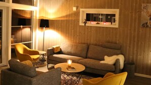 Ein modernes Wohnzimmer mit Holzwand, einer Couch, zwei Sesseln, einem Couchtisch und einer Stehlampe.