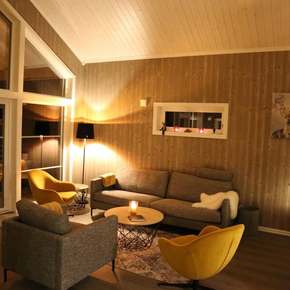 Un salon moderne avec un mur en bois, un canapé, deux fauteuils, une table basse et un lampadaire.