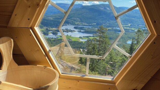 Ein Holzinnenraum mit einem sechseckigen Dachfenster mit Blick auf einen See und Berge.
