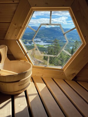 Un intérieur en bois agrémenté d’une lucarne hexagonale donnant sur un lac et des montagnes.