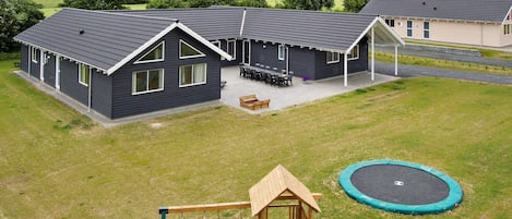 A residential property with a house, a patio with outdoor furniture, a swing set, and a trampoline.