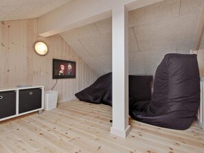 A room with a sloped ceiling, a television mounted on the wall, a white column, and a black bean bag chair. - 5 Star Holiday Home in Bogense (Bogense)