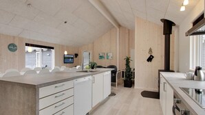 Moderni keittiö, jossa on keskeinen saareke, valkoiset kaapit ja puinen katto.