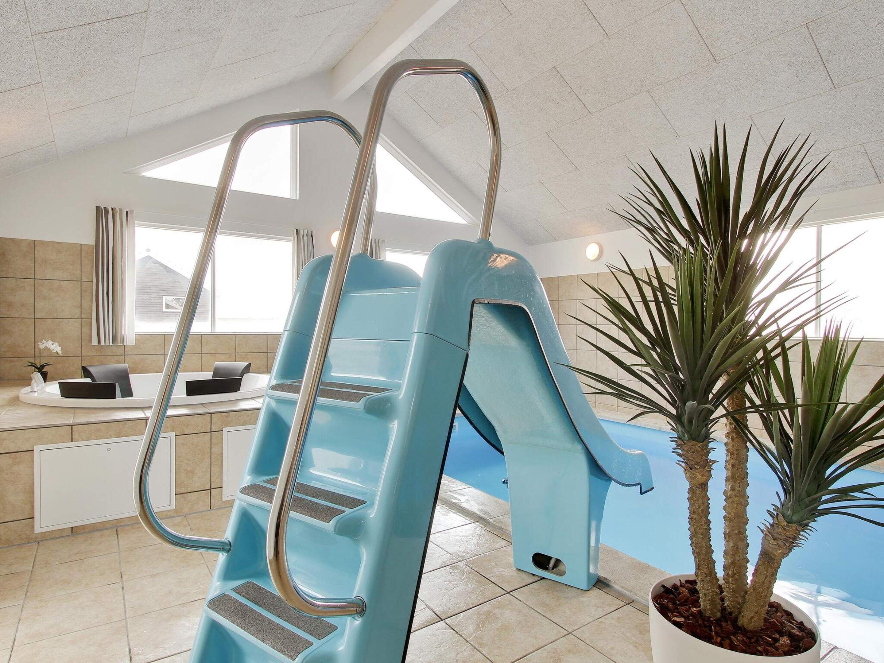 A pool area with a blue slide, a potted plant, and a window with curtains.