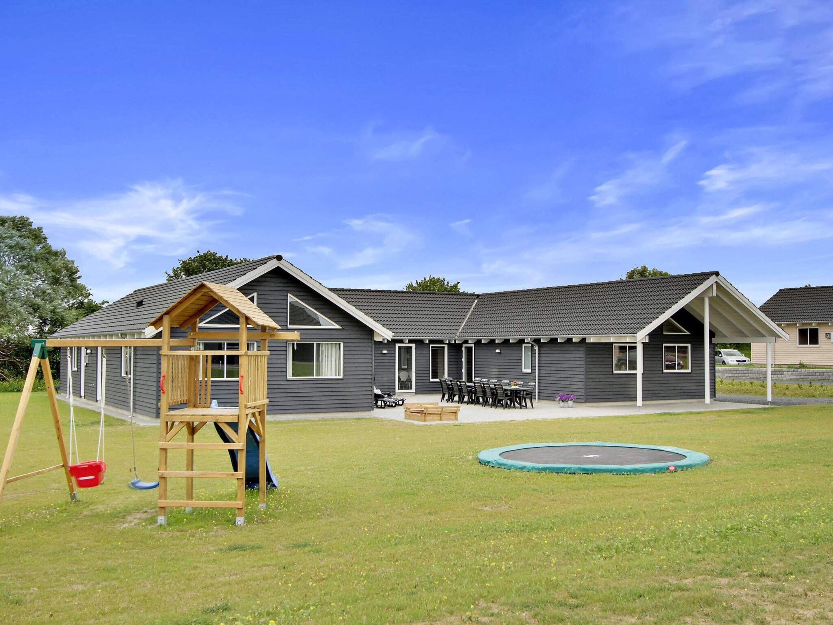 A residential building with a covered patio, a swing set, and a trampoline in the yard.
