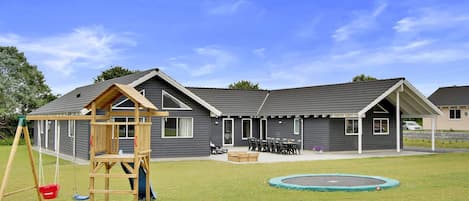 A residential building with a covered patio, a swing set, and a trampoline in the yard.