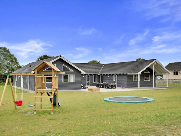 A residential building with a covered patio, a swing set, and a trampoline in the yard.