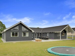 A two-story building with a flat roof, a covered patio area with outdoor seating, and a trampoline in the foreground.