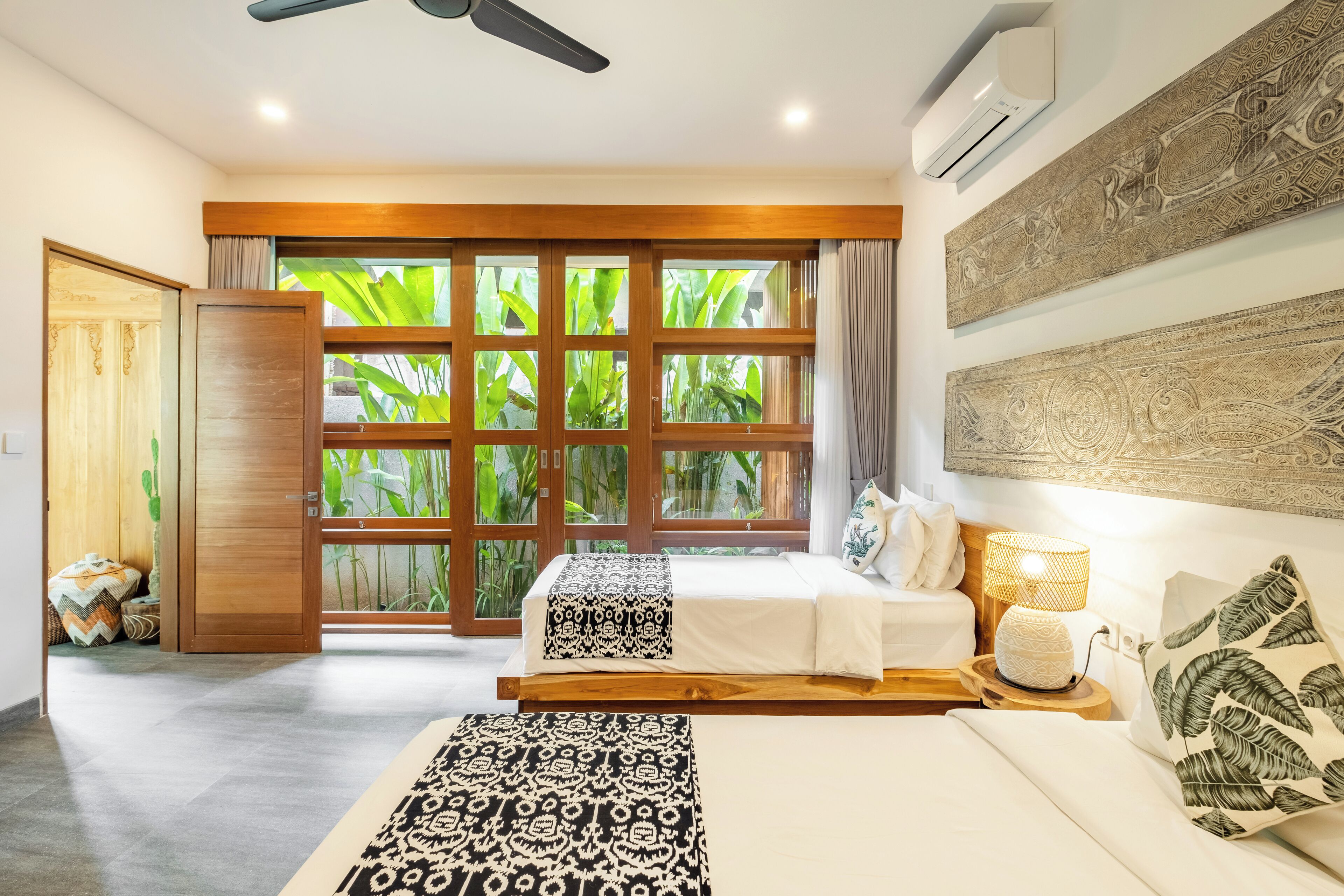 A hotel room with a large window, a ceiling fan, and a bed with a patterned bedspread.