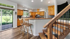 Una cocina moderna con armarios de madera, una isla central con taburetes altos y una escalera con barandilla de madera.