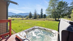 Un jacuzzi en una terraza de madera con vistas a un campo verde y montañas al fondo.