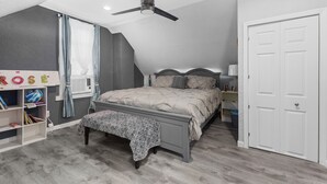 Un dormitorio con cama, ventilador de techo, estantería y puerta.