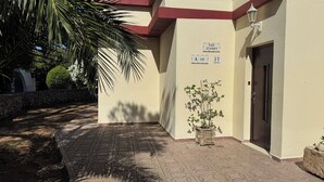A building entrance with a palm tree, a potted plant, and a sign reading "Los Juanes A-142 37".