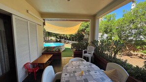Un patio techado con piscina, mobiliario exterior y vista al jardín trasero.
